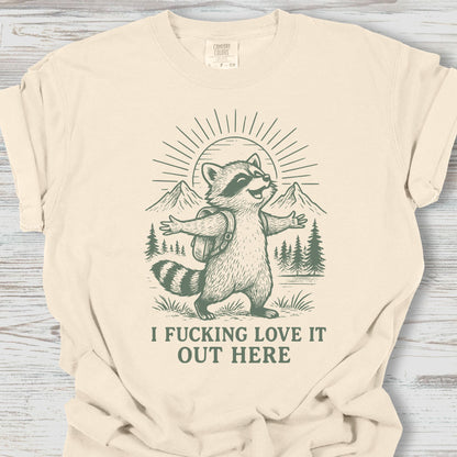 Beige t-shirt with a raccoon graphic and text on a wooden surface
