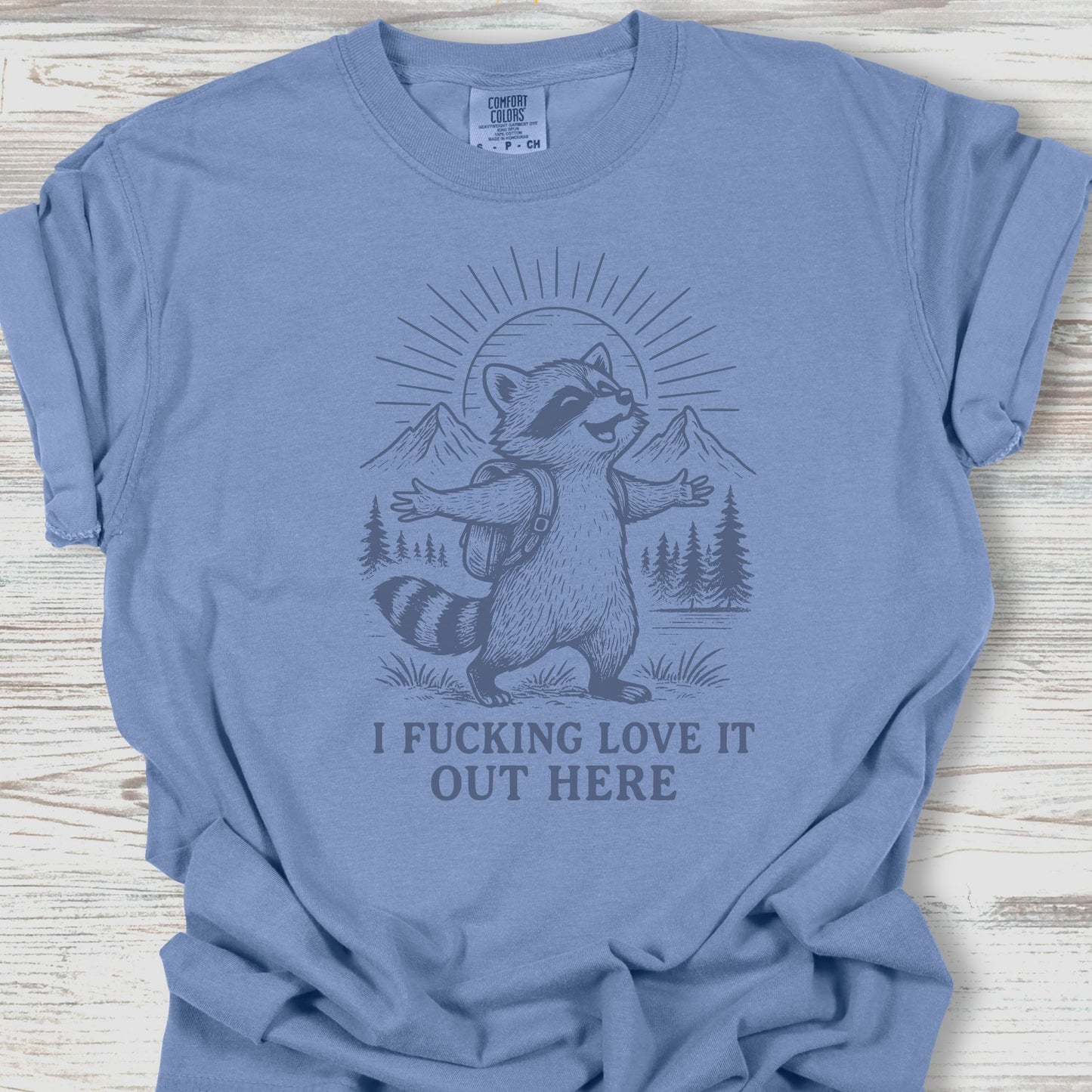 Blue t-shirt with a raccoon graphic and text on a wooden surface