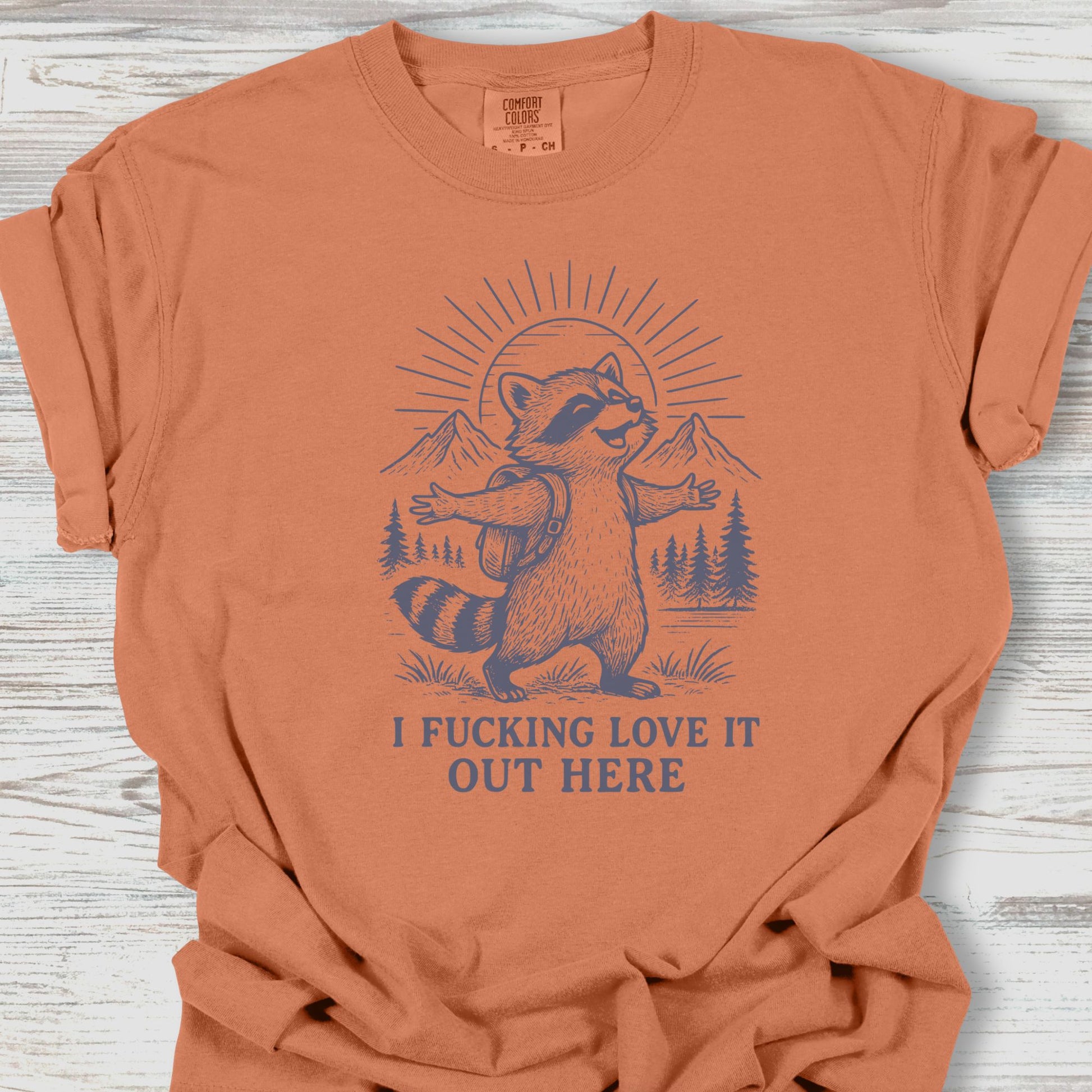 Orange t-shirt with a raccoon graphic and text on a wooden surface