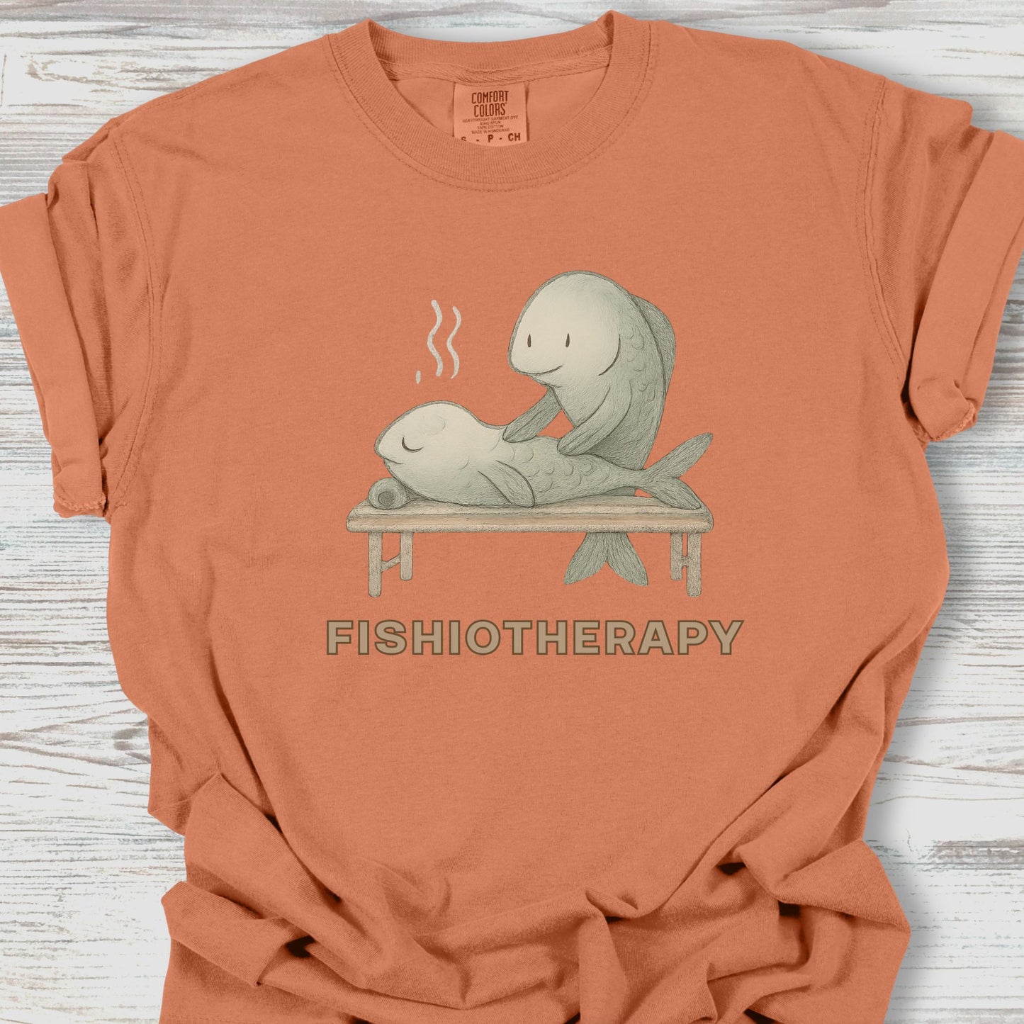 Orange t-shirt with 'Fishiotherapy' graphic on a wooden surface