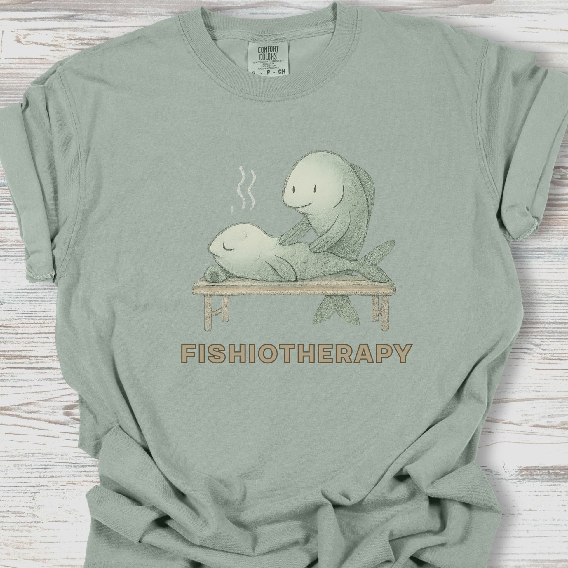 Sage green t-shirt with 'Fishiotherapy' graphic on a wooden surface