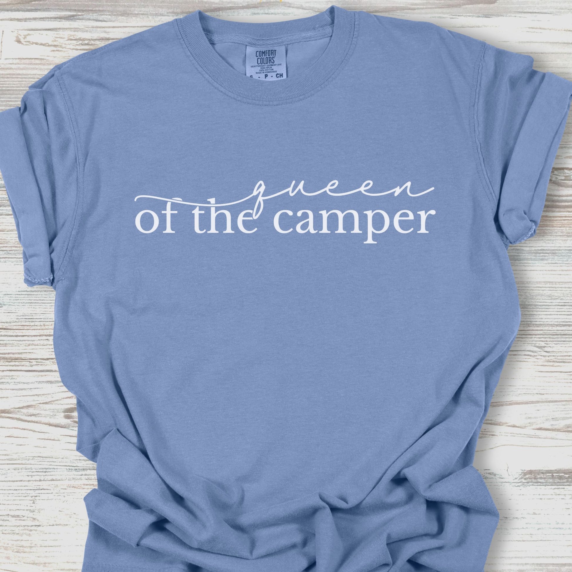 Blue t-shirt with 'Queen of the Camper' text on a wooden surface