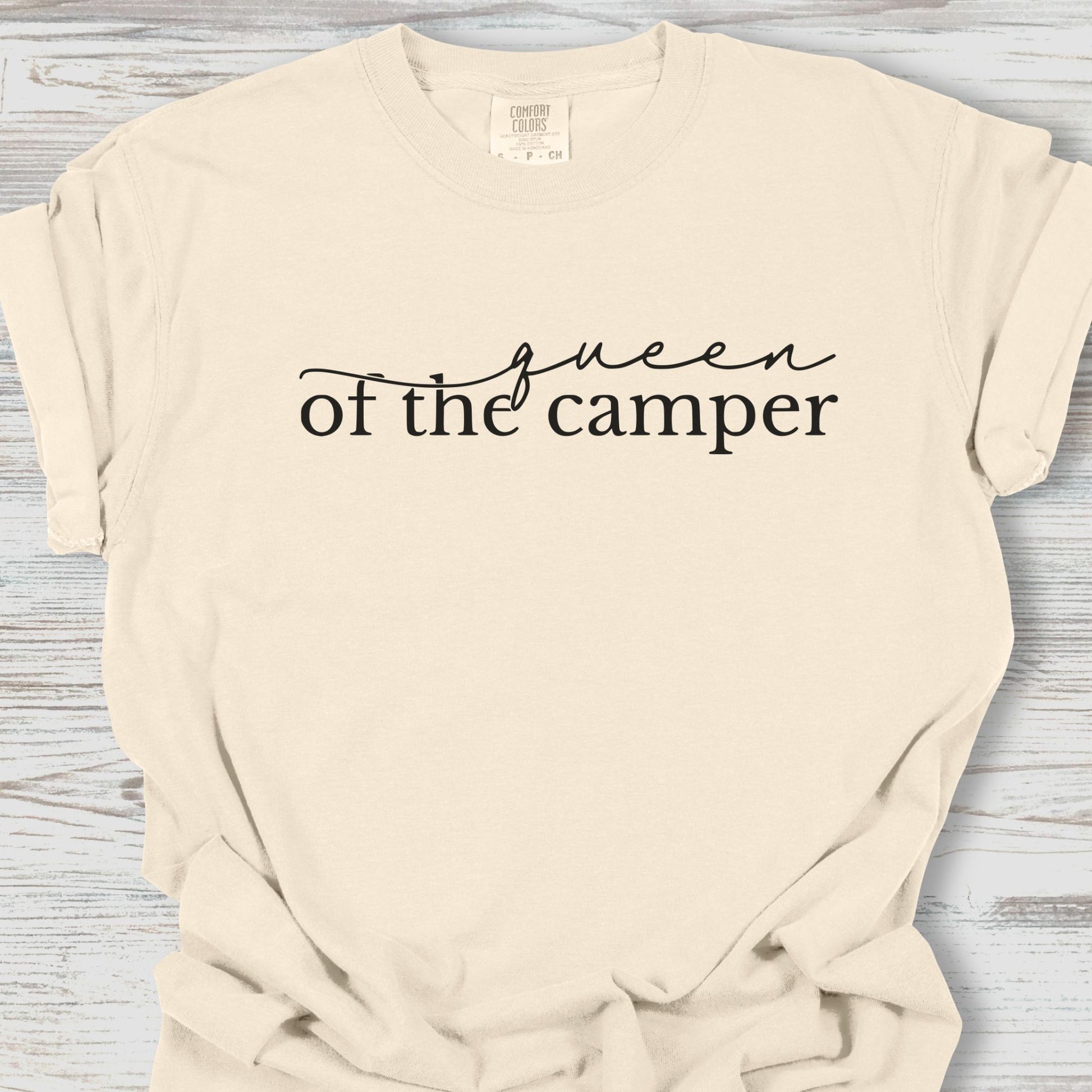 Beige t-shirt with 'Queen of the Camper' text on a wooden surface