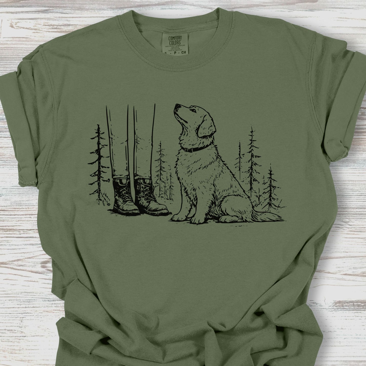 Green t-shirt with a graphic of a dog, boots, and trees on a wooden surface