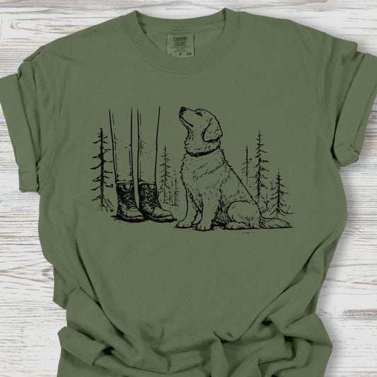 Green t-shirt with a graphic of a dog, boots, and trees on a wooden surface
