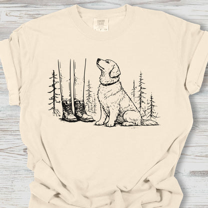 Beige t-shirt with a graphic of a dog, boots, and trees on a wooden surface