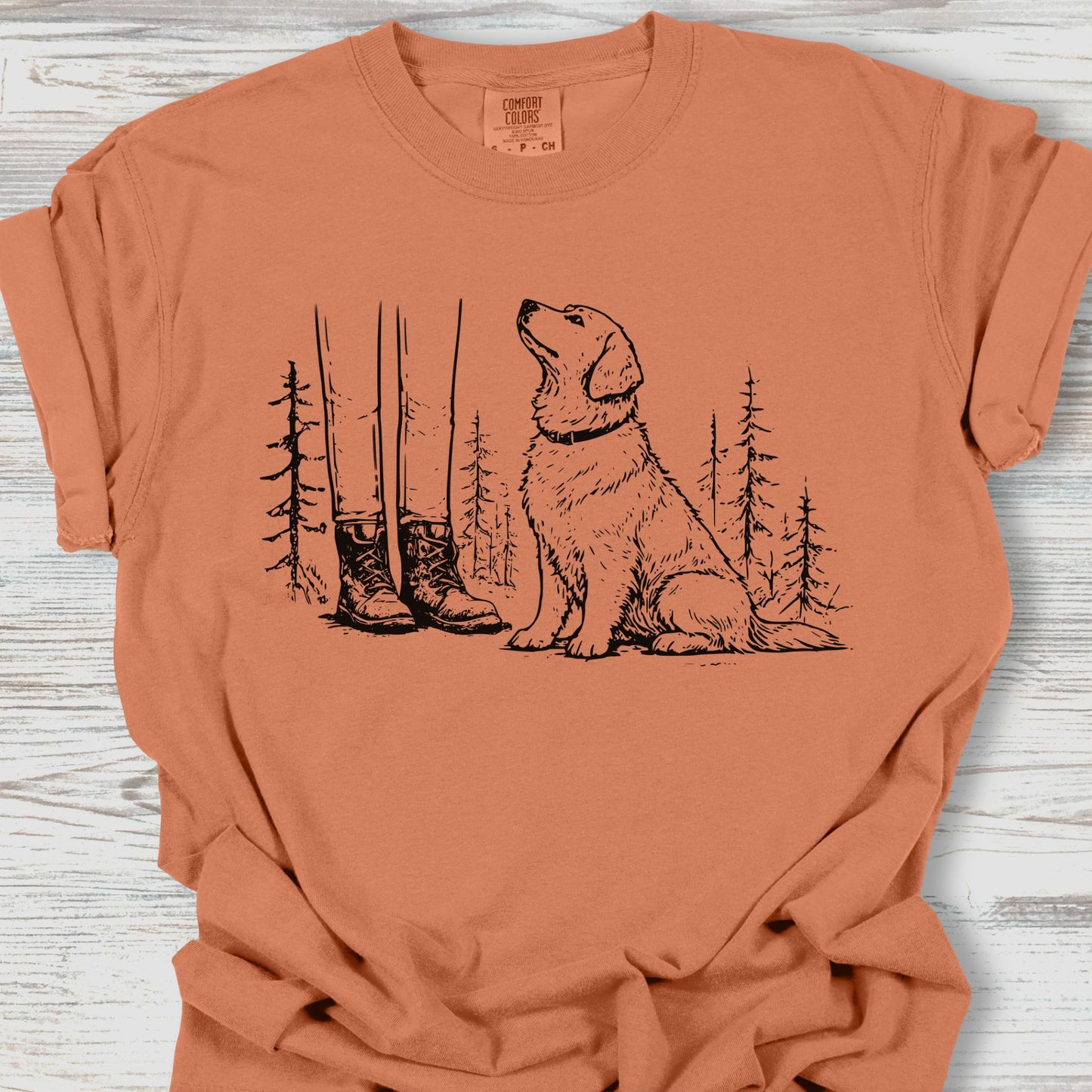 Coral t-shirt with a dog and forest graphic on a wooden surface