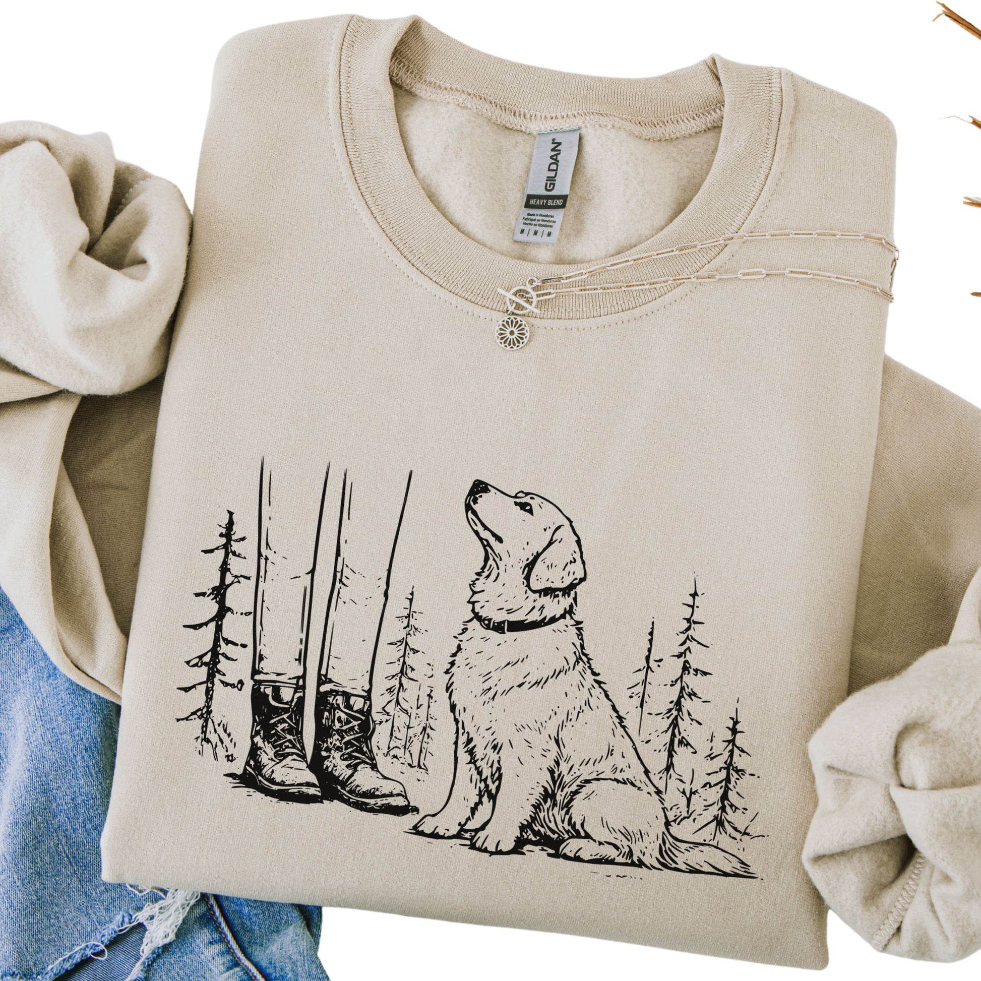 Beige sweatshirt with a dog and forest design, held by two hands.