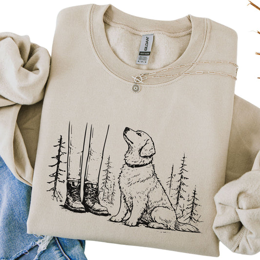 Beige sweatshirt with a dog and forest design, held by two hands.