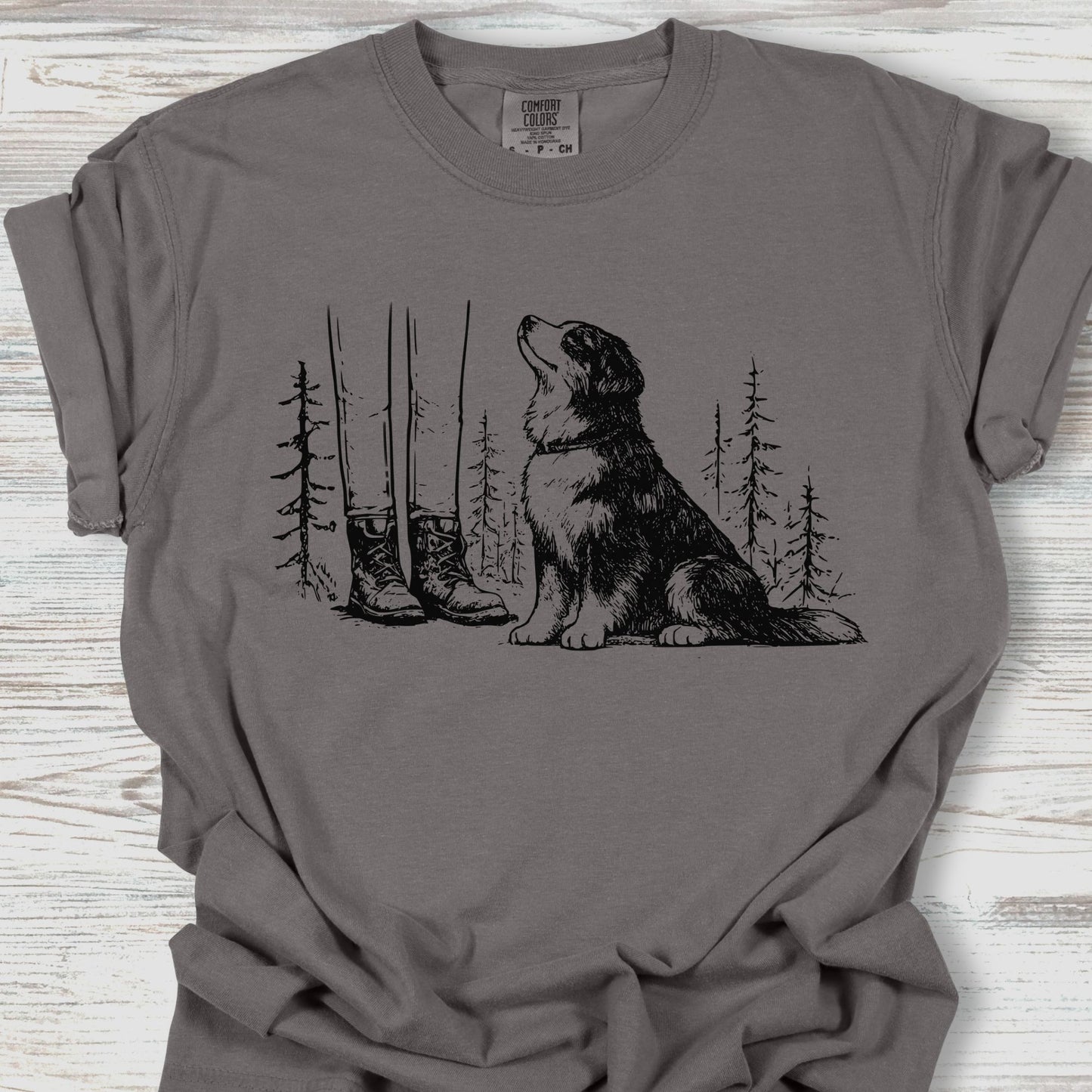 Gray t-shirt with a graphic of a dog, boots, and trees on a wooden surface
