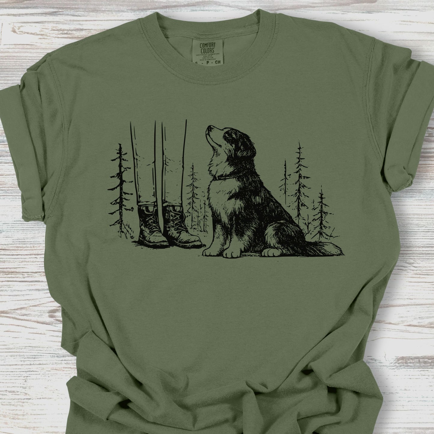 Green t-shirt with a graphic of a dog and boots in a forest on a wooden surface