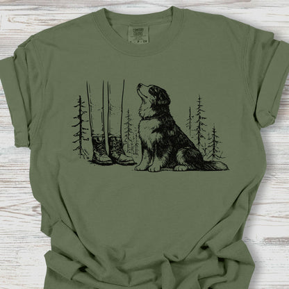 Green t-shirt with a graphic of a dog and boots in a forest on a wooden surface