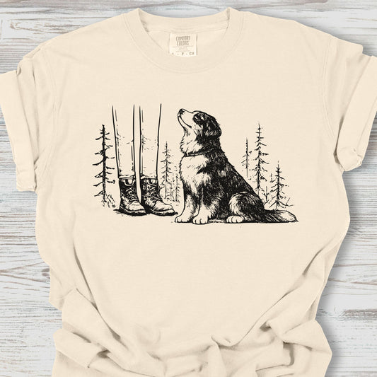 Beige t-shirt with a graphic of a dog and boots in a forest on a wooden surface