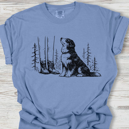 Blue t-shirt with a graphic of a dog, boots, and trees on a wooden surface