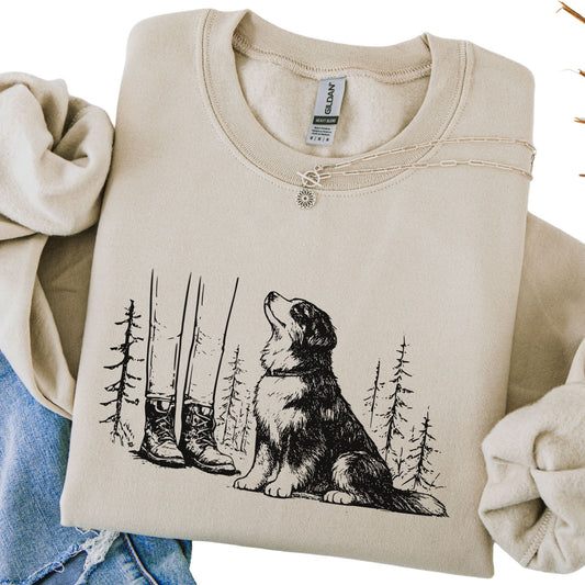 Beige sweatshirt with a dog and forest design, held by two hands.