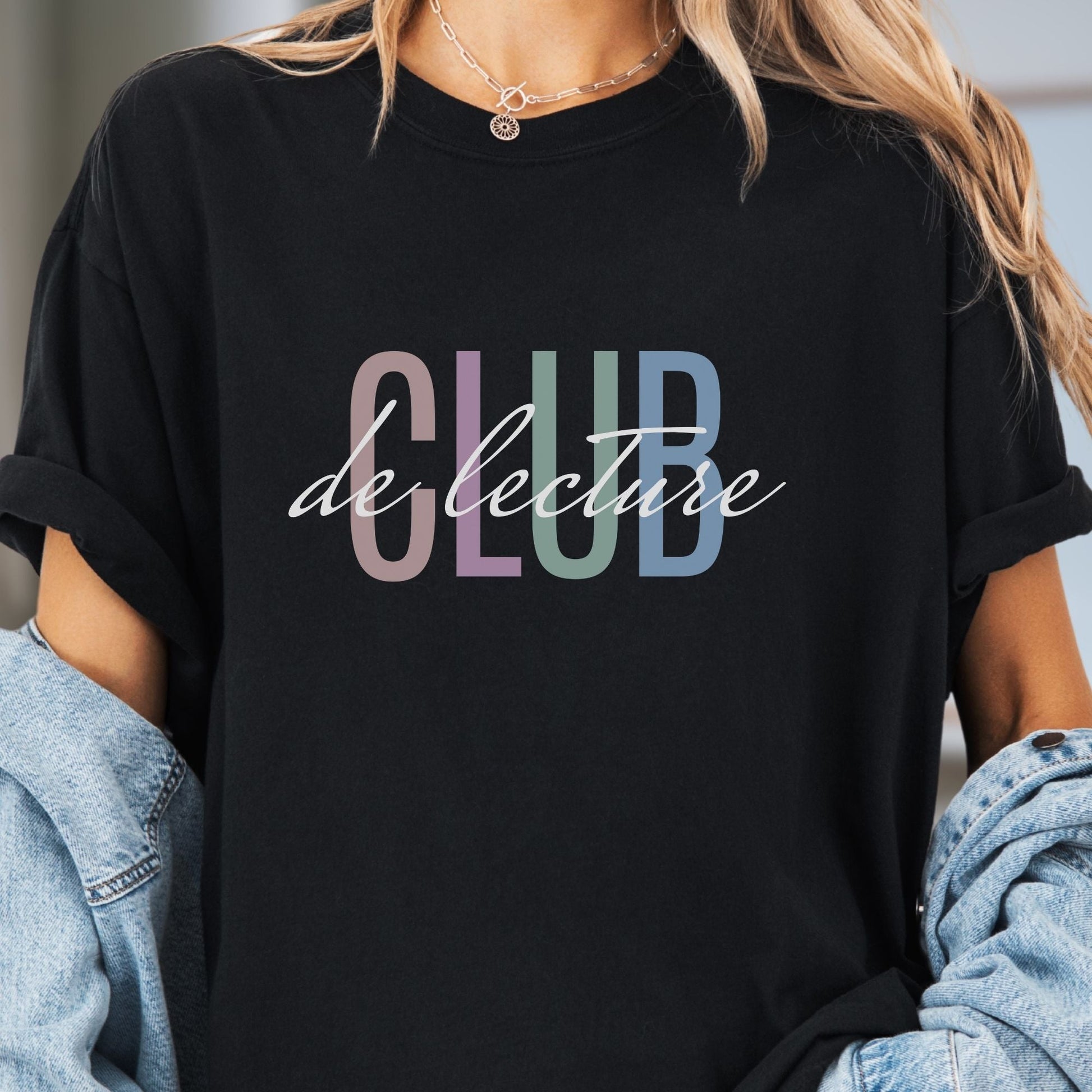 Model wears a black colored t-shirt with the words CLUB de lecture (French for Book Club).  The word CLUB is in large printed font in pastel colors. The words de lecture are handwritten font in black and are printed on top of the word Club.