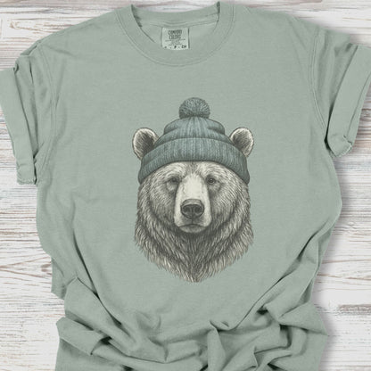 Sage green t-shirt with a bear wearing a beanie graphic on a wooden surface