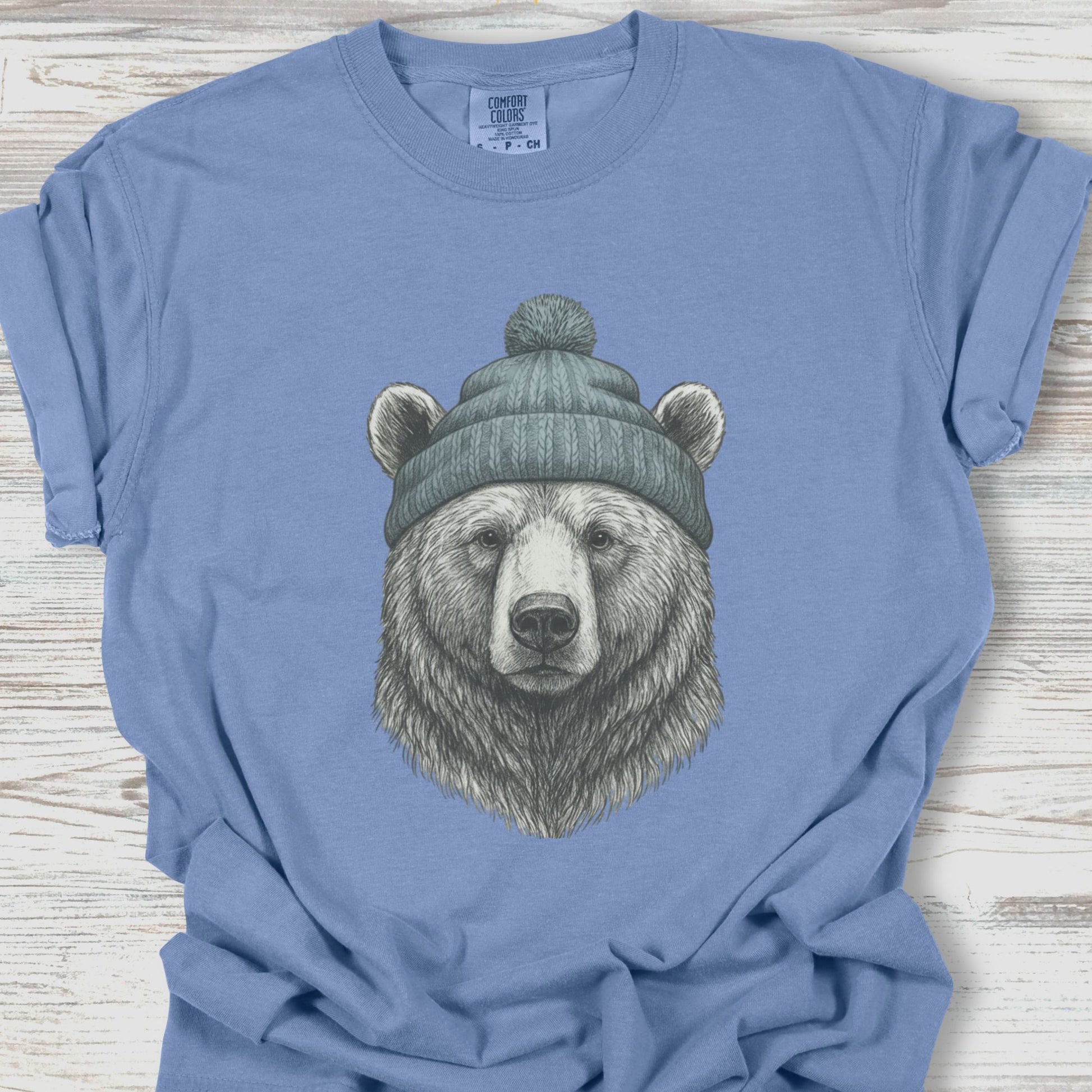 Blue t-shirt with a bear wearing a beanie graphic on a wooden surface