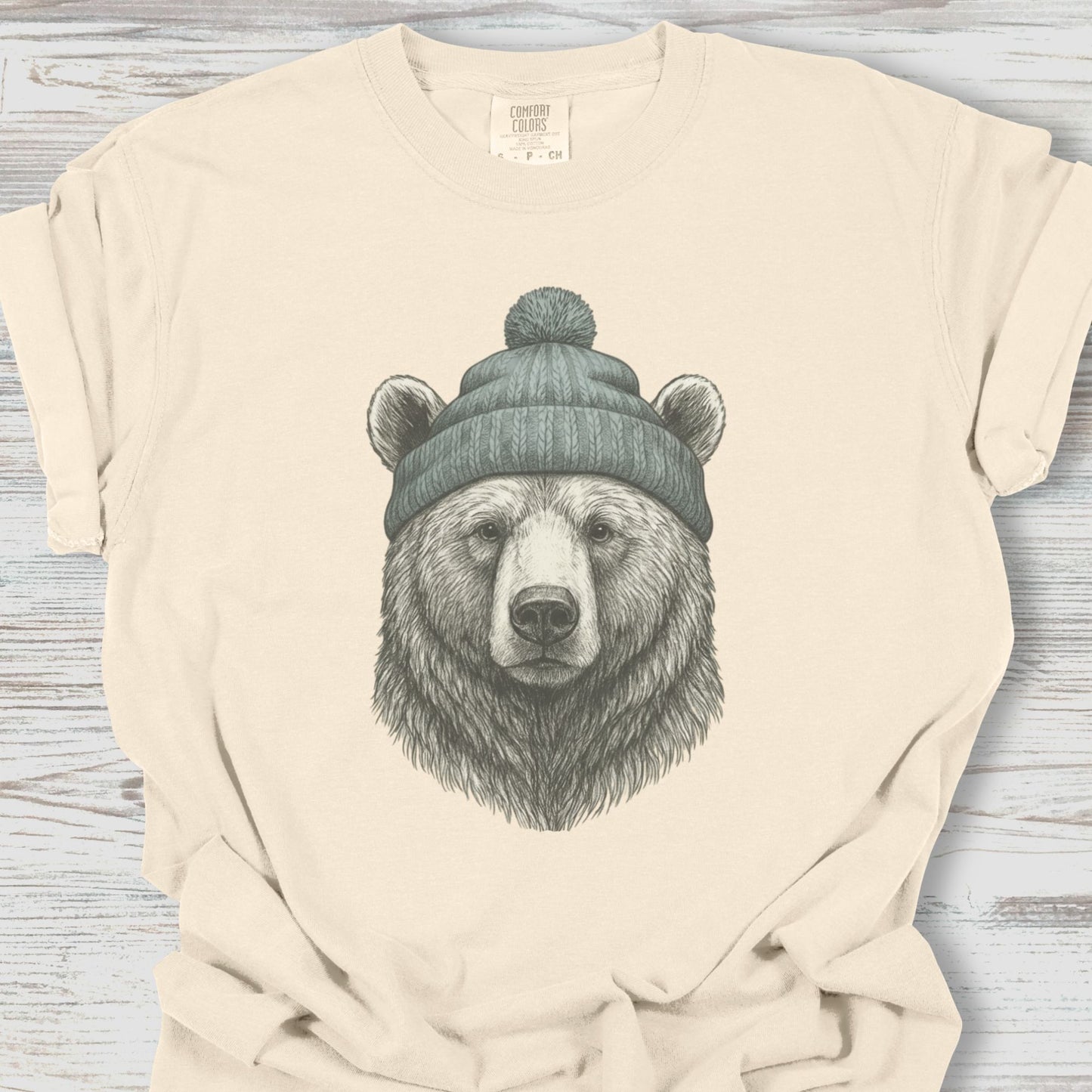 Beige t-shirt with a bear wearing a beanie graphic on a wooden surface