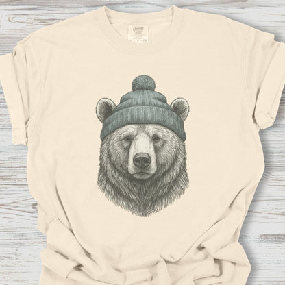 Beige t-shirt with a bear wearing a beanie graphic on a wooden surface