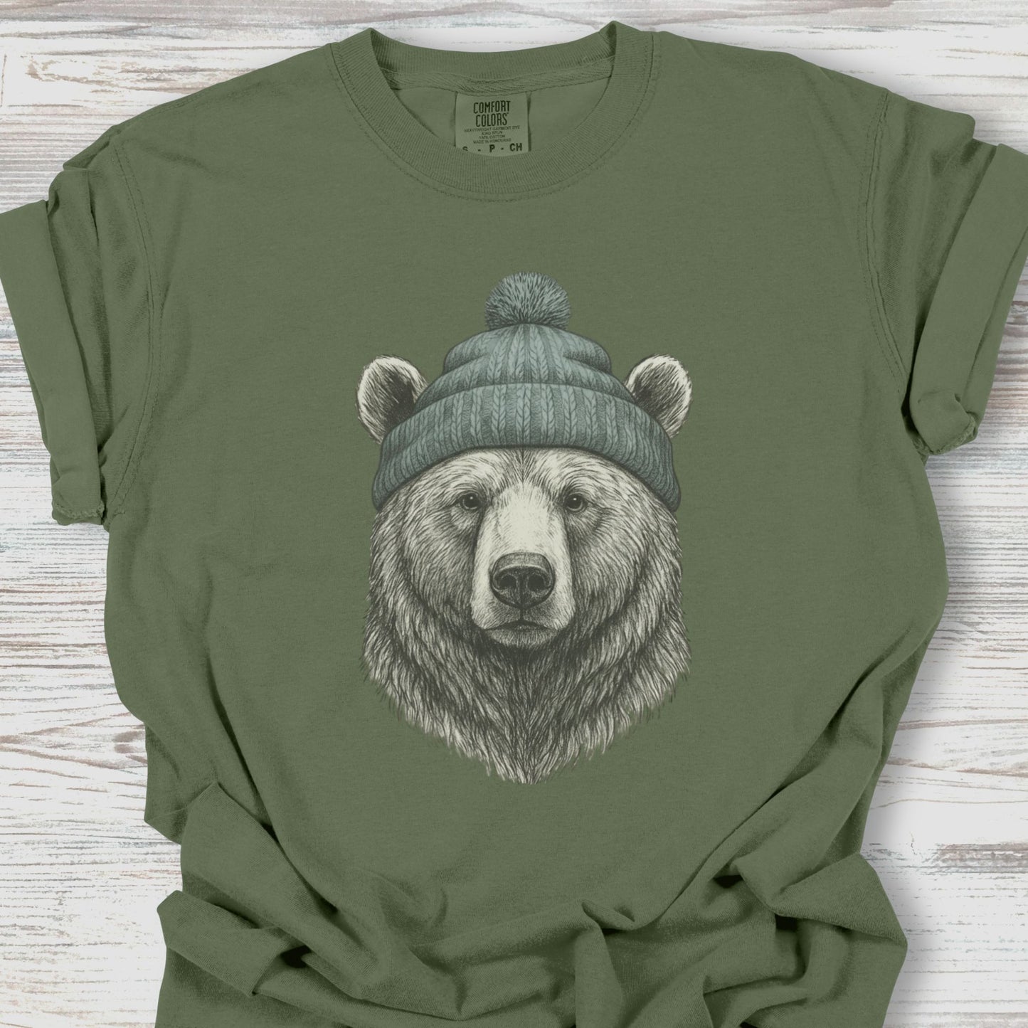 Green t-shirt with a bear wearing a beanie graphic on a wooden surface