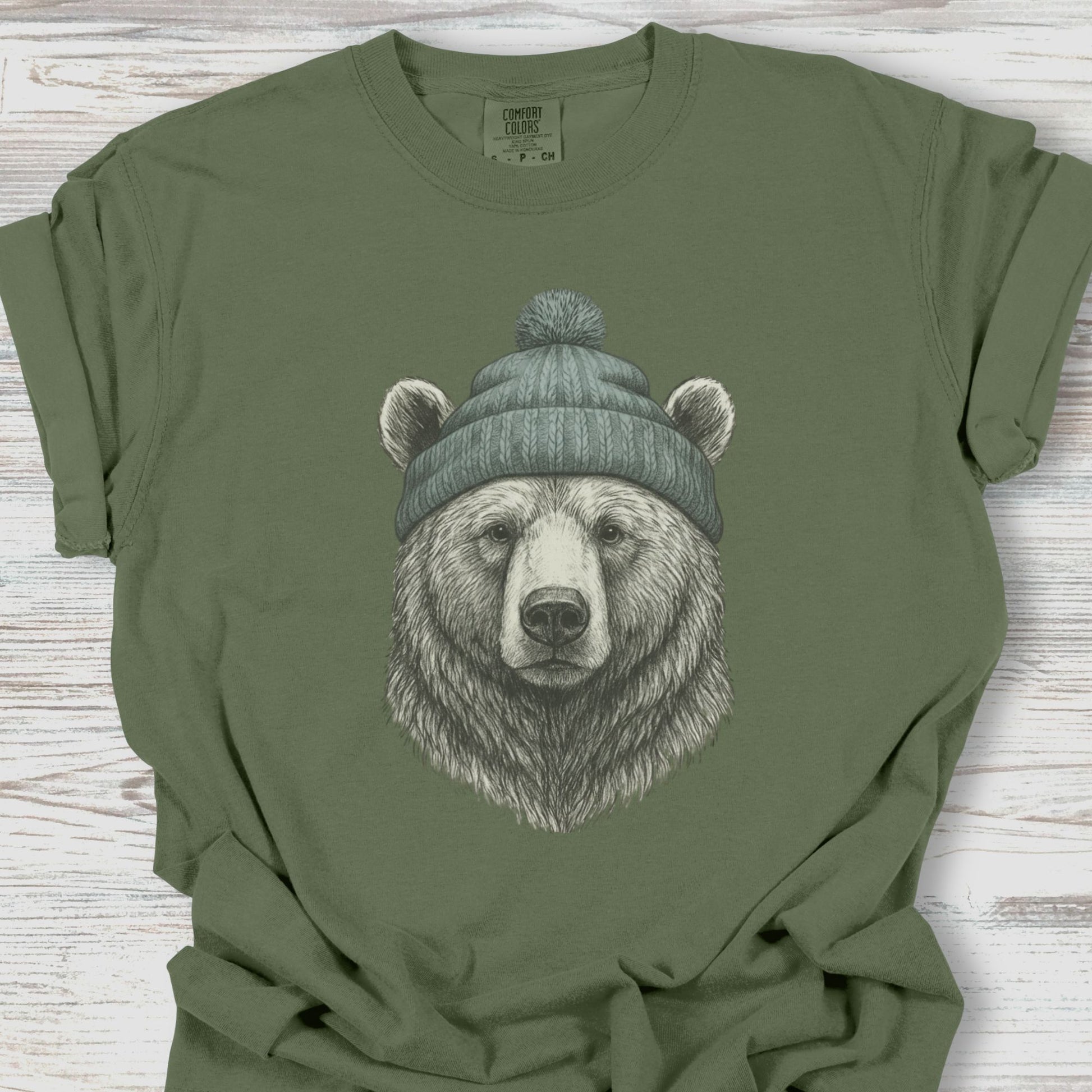 Green t-shirt with a bear wearing a beanie graphic on a wooden surface