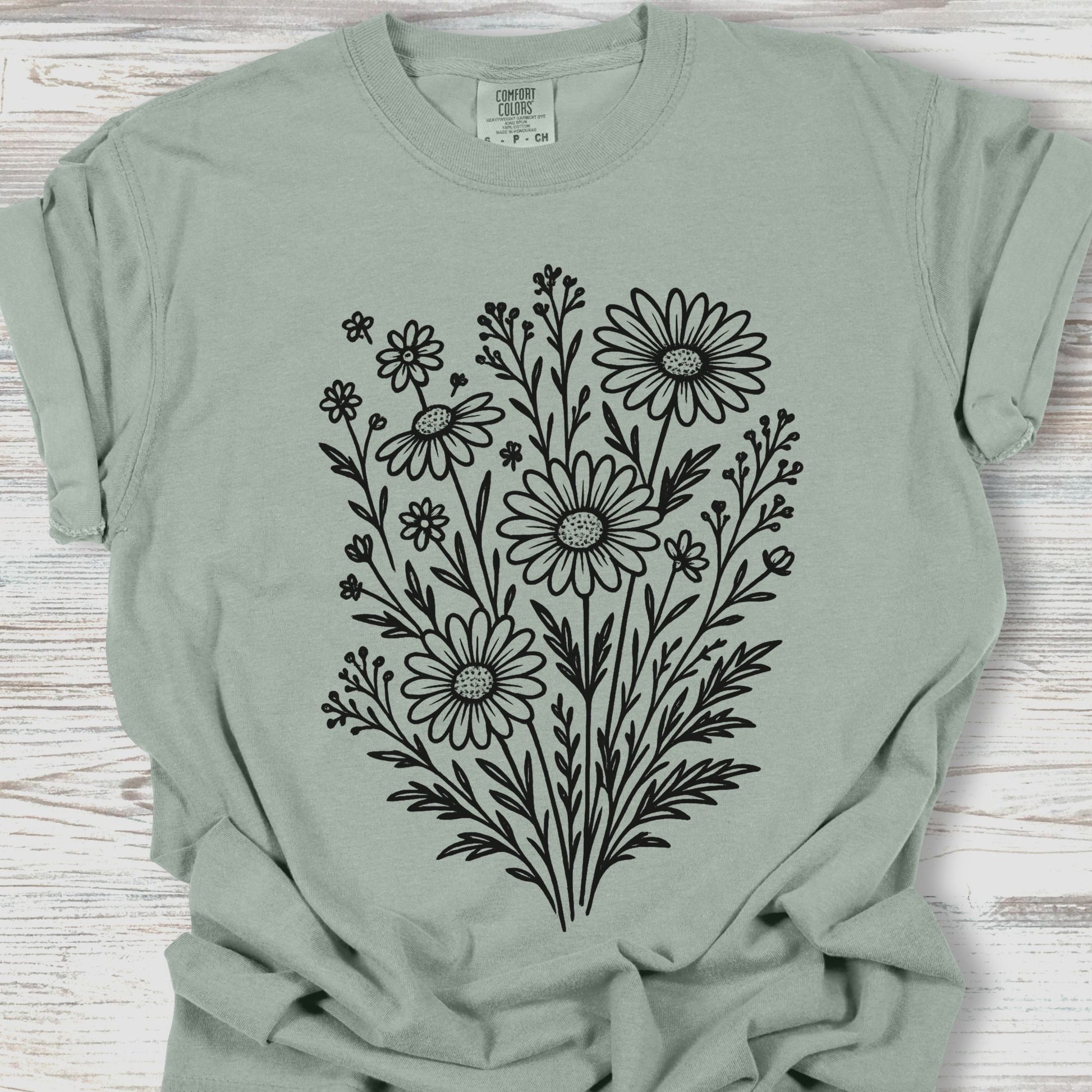 Sage green t-shirt with black floral design on a wooden surface