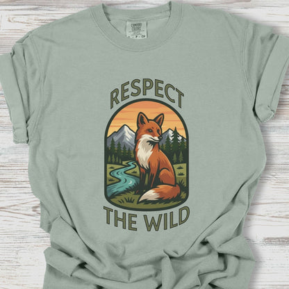 Sage green t-shirt with a fox graphic and 'Respect the Wild' text on a wooden surface