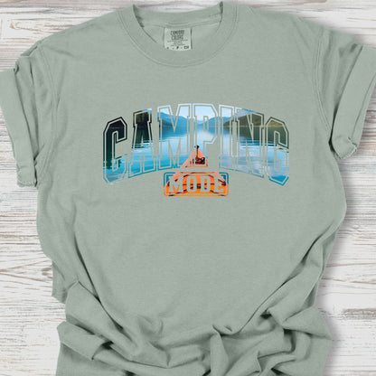 Sage green t-shirt with 'Camping Mode' graphic on a wooden surface
