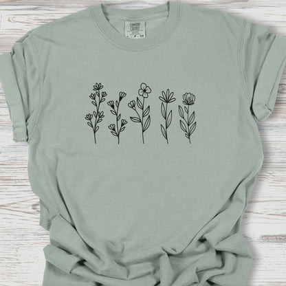 Sage green t-shirt with black floral designs on a wooden surface