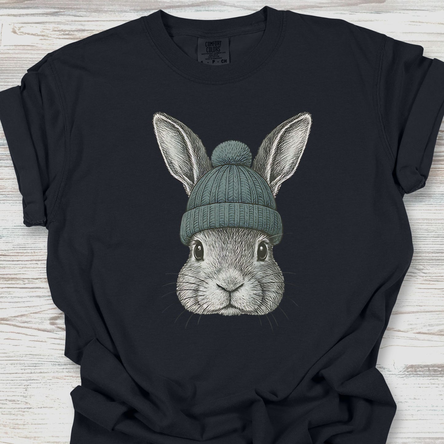 Black t-shirt with a graphic of a rabbit wearing a green beanie on a wooden surface
