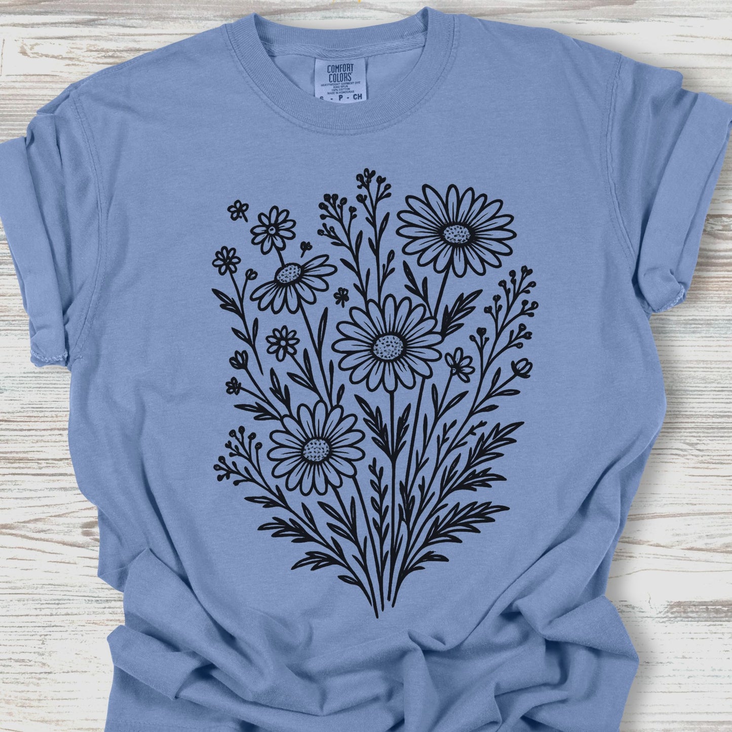 Blue t-shirt with black floral design on a wooden surface