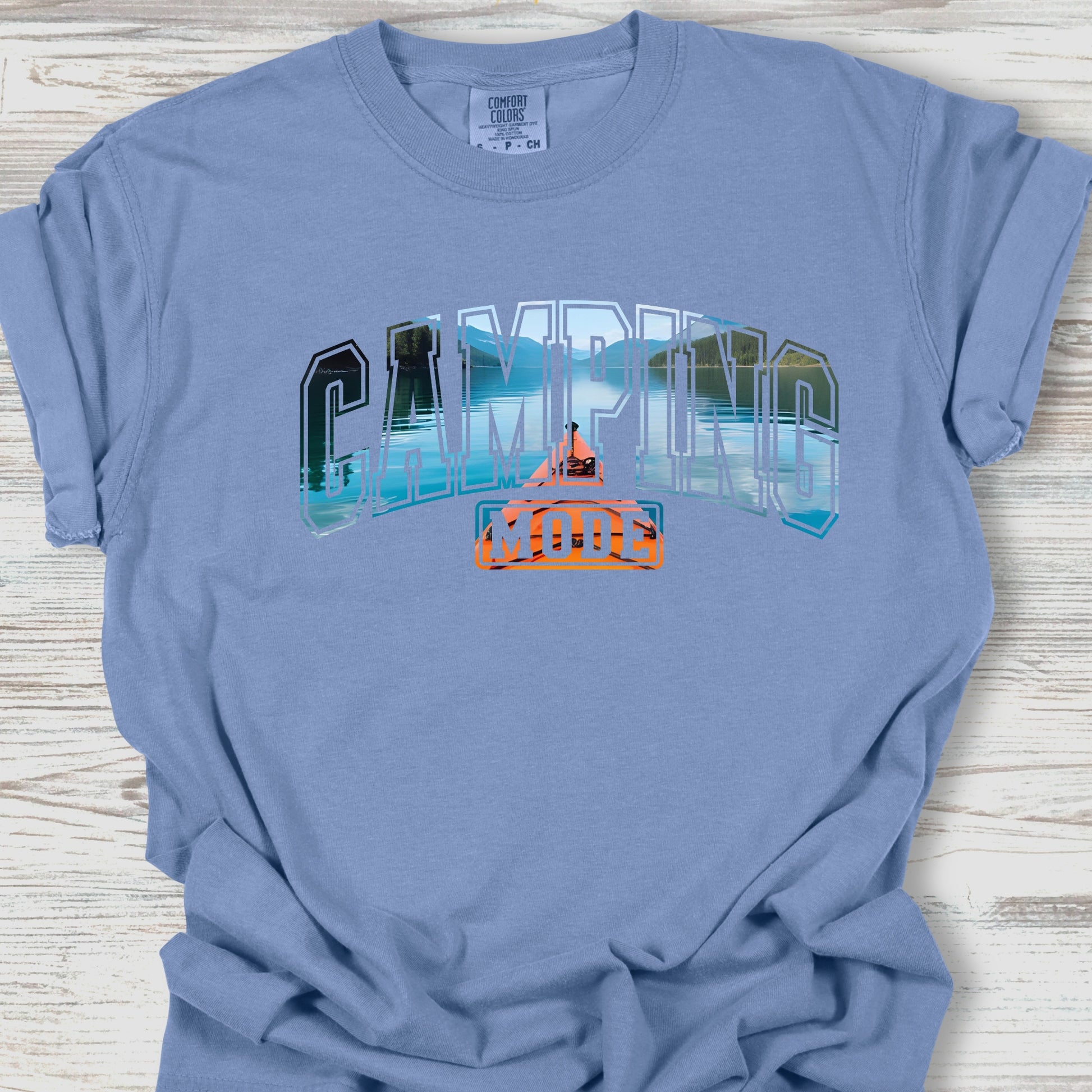 Blue t-shirt with 'Camping Mom' graphic on a wooden surface