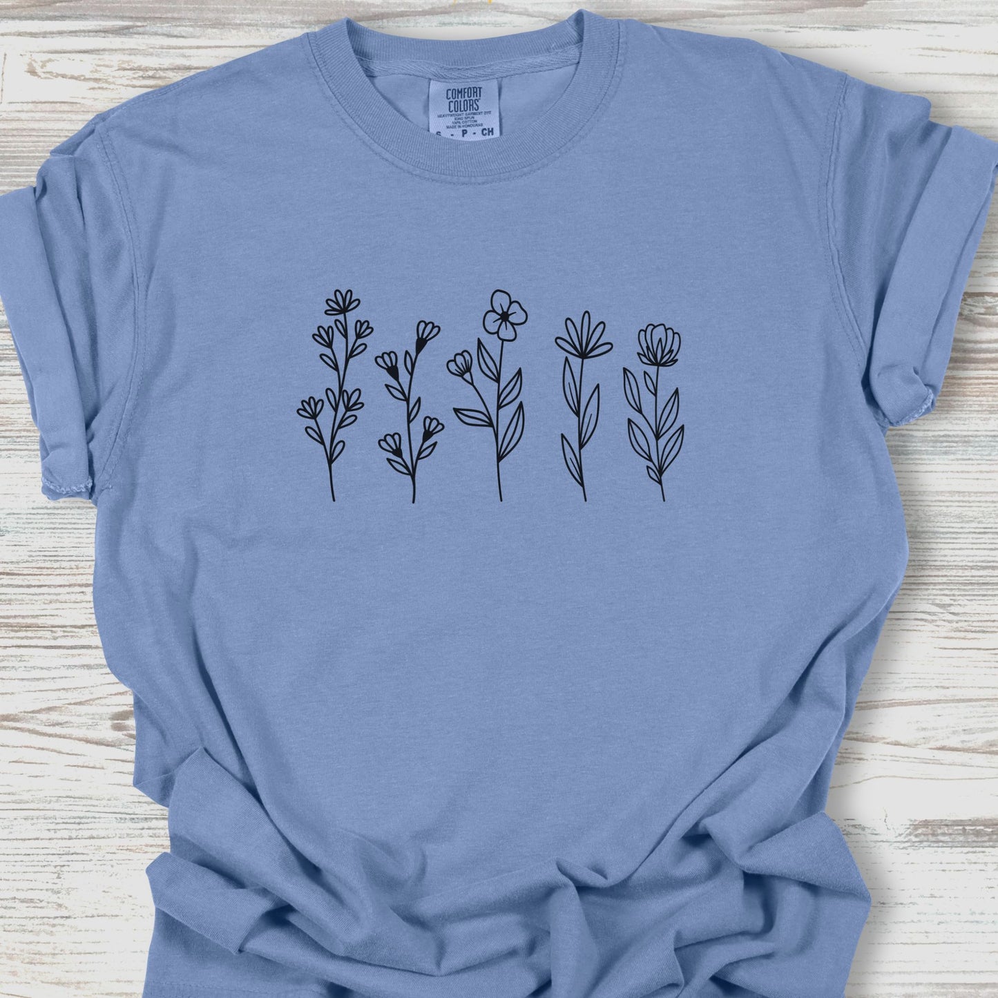 Blue t-shirt with black floral designs on a wooden surface