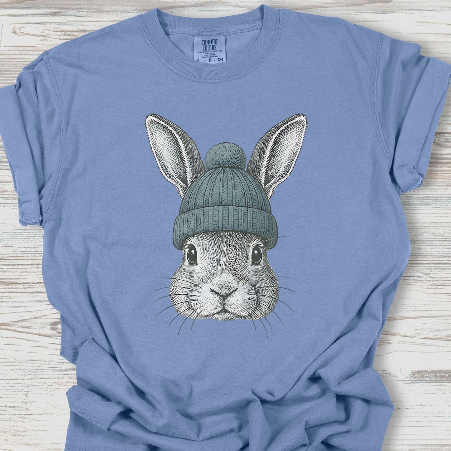 Blue t-shirt with a graphic of a rabbit wearing a green beanie on a wooden surface