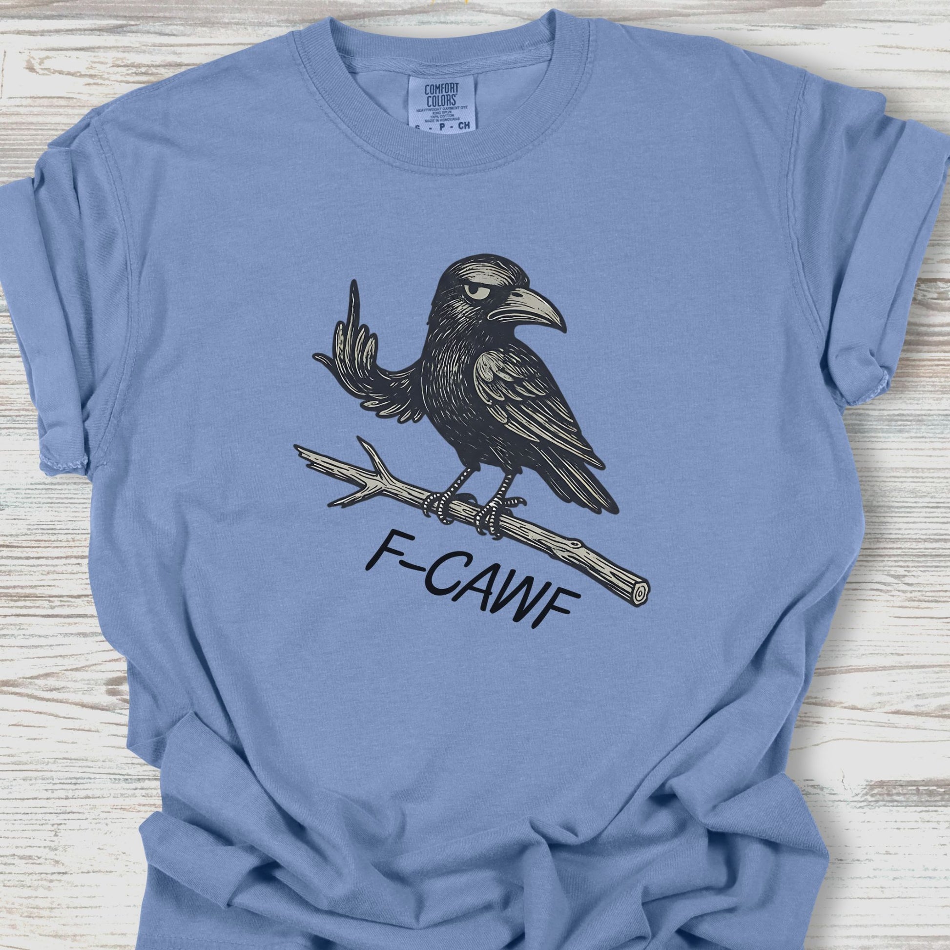 Blue t-shirt with a black crow graphic and 'F-CAWF' text on a wooden surface