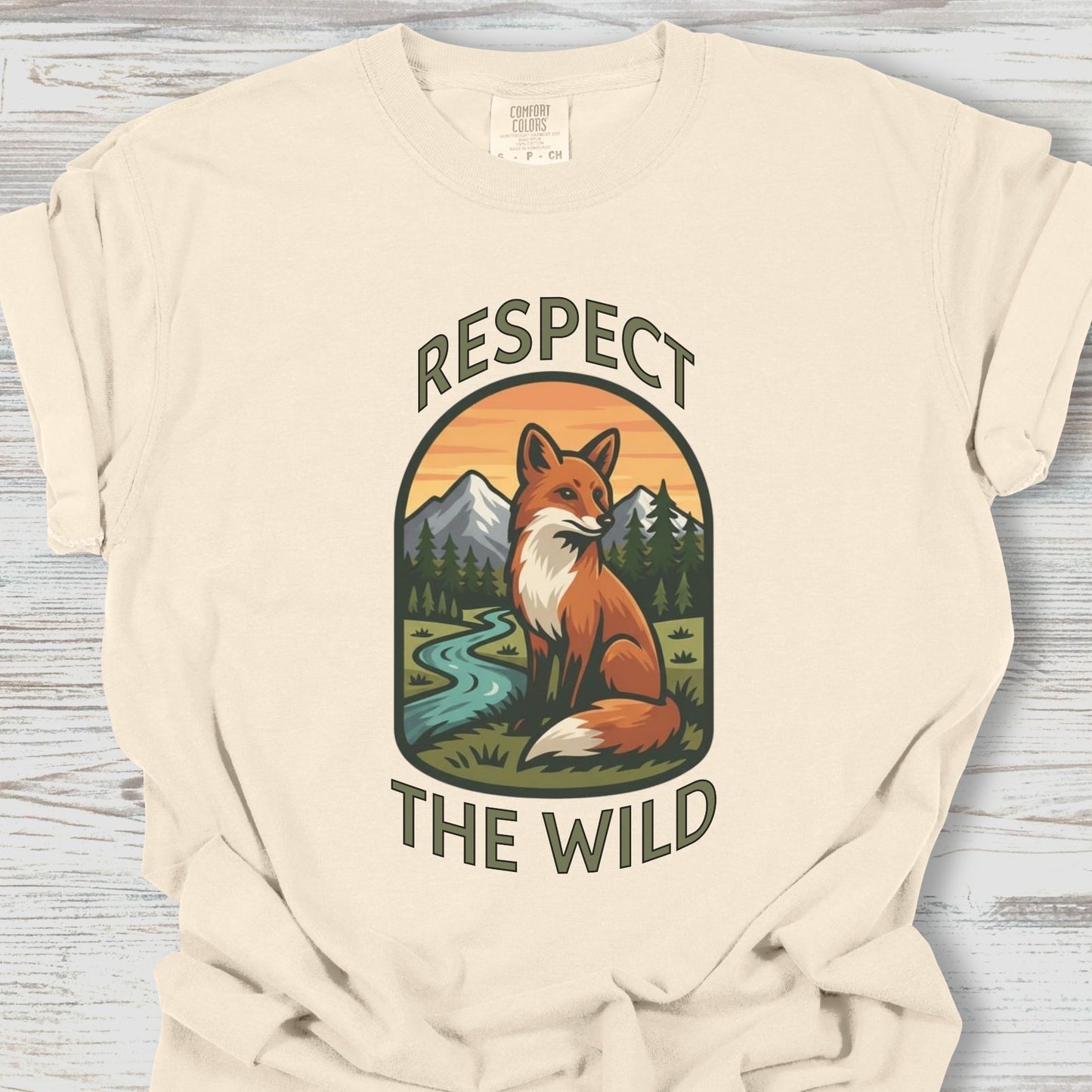 Beige t-shirt with a fox graphic and 'Respect the Wild' text on a wooden surface