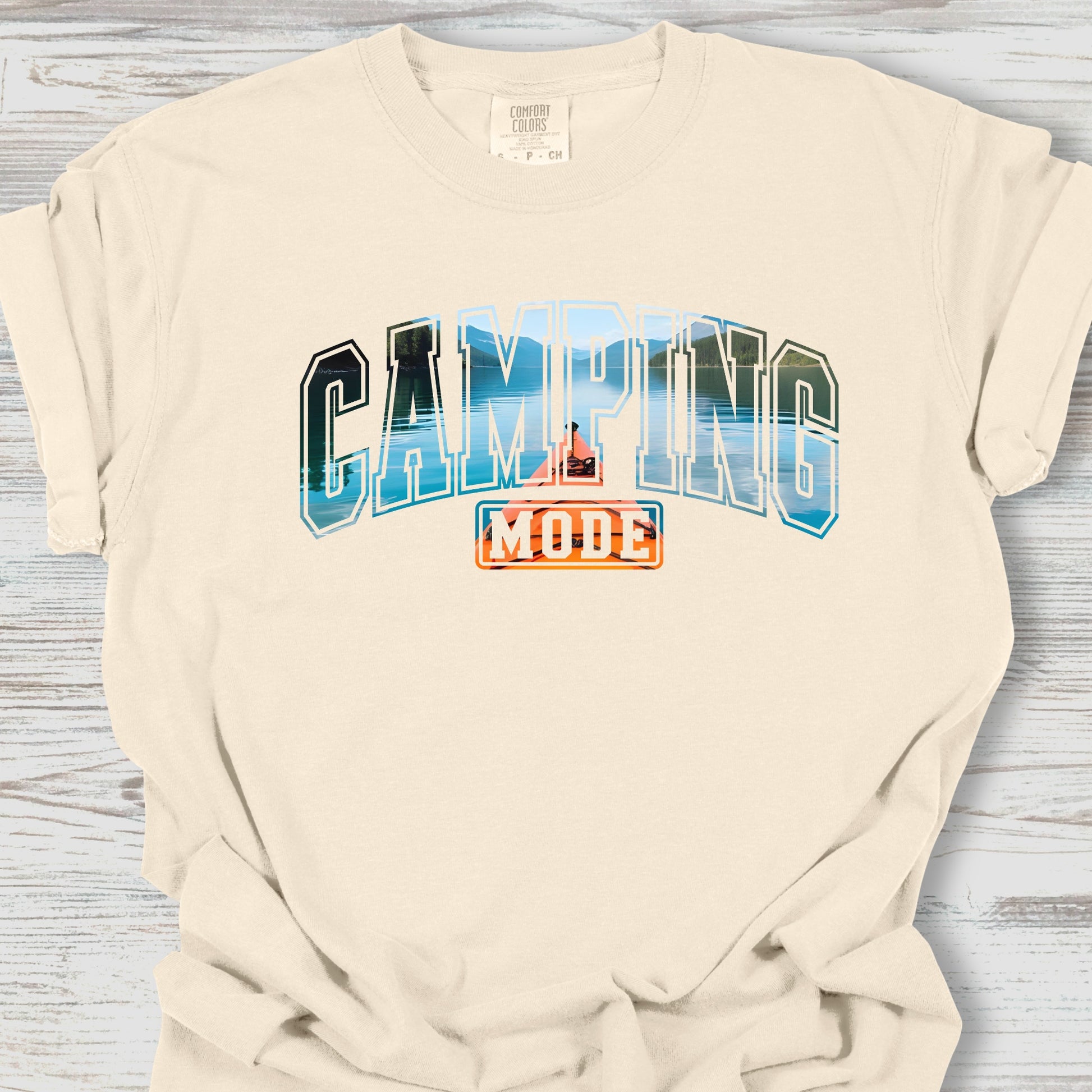 Beige t-shirt with 'Camping Mode' graphic on a wooden surface