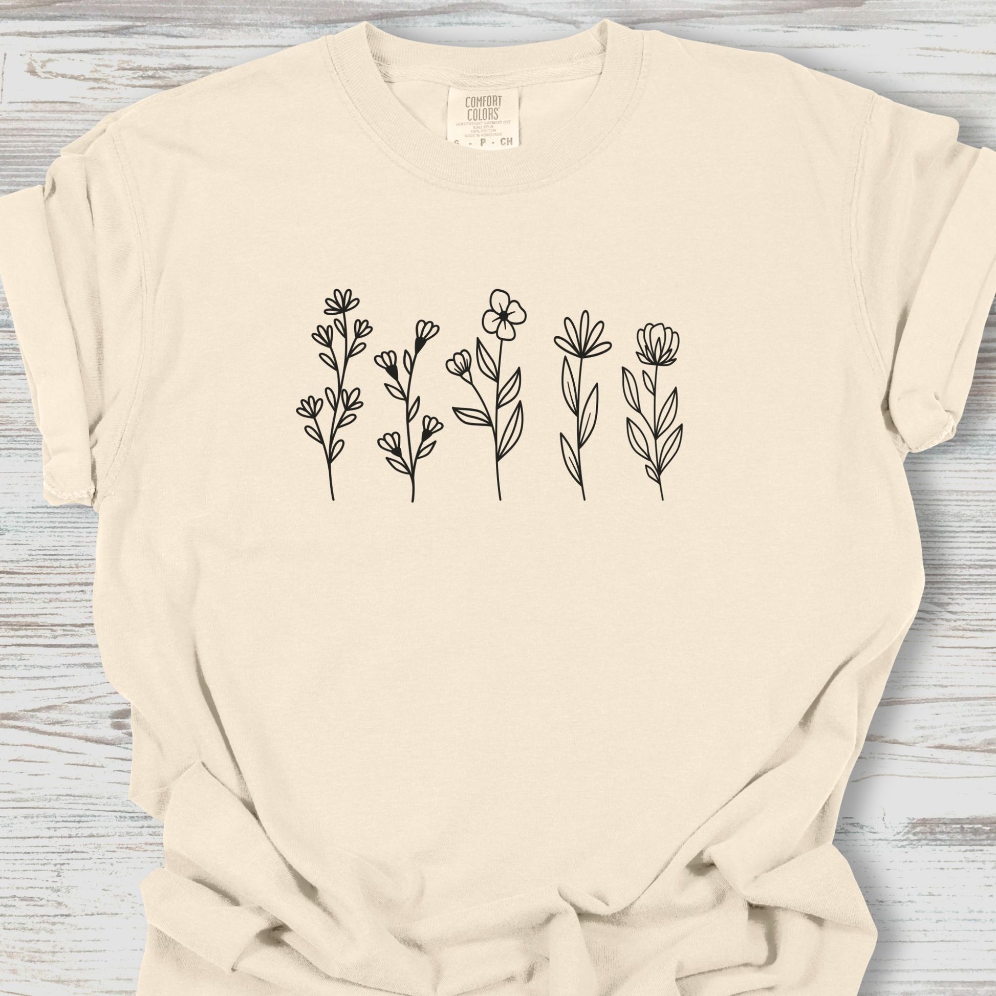 Beige t-shirt with black floral designs on a wooden surface