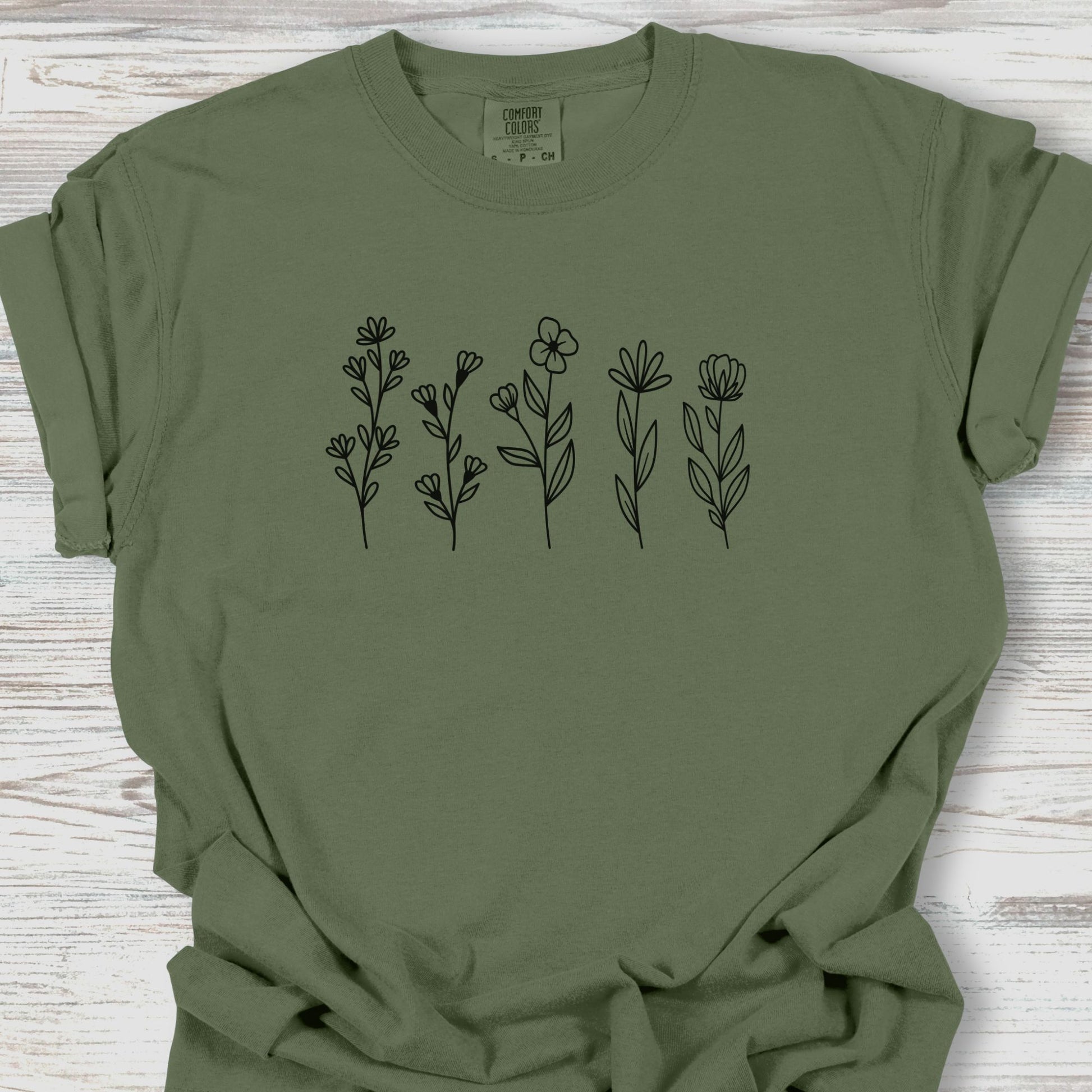 Green t-shirt with black floral designs on a wooden surface
