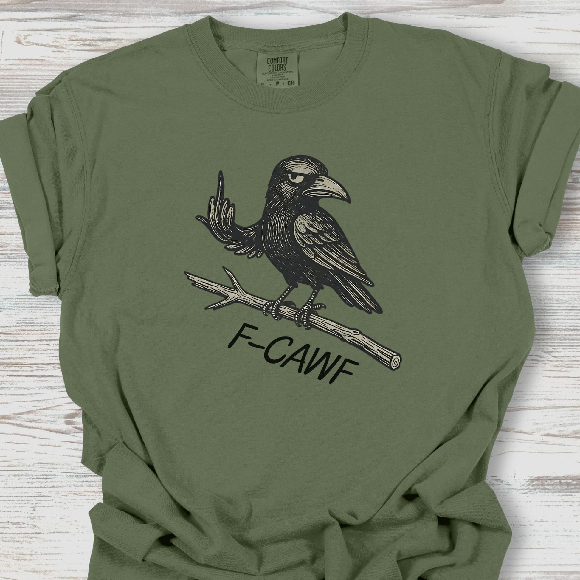 Green t-shirt with a black crow graphic and 'F-CAWF' text on a wooden surface