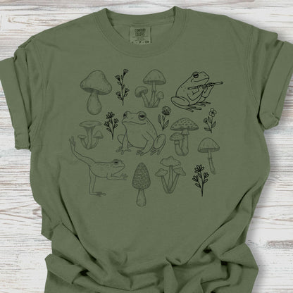 Green t-shirt with black frog and mushroom design on a wooden surface