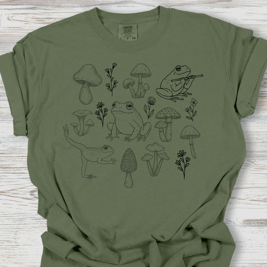 Green t-shirt with black frog and mushroom design on a wooden surface