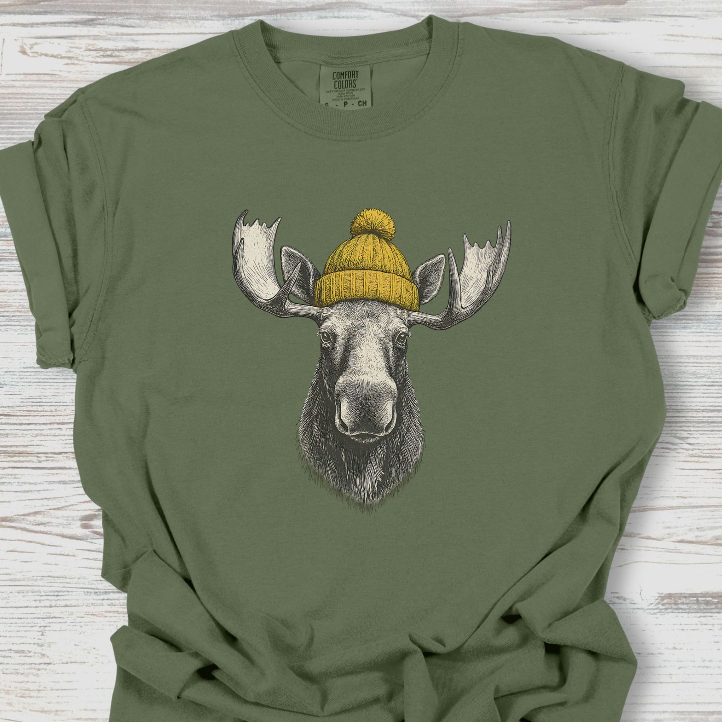 Green t-shirt with a moose wearing a yellow beanie on a wooden surface