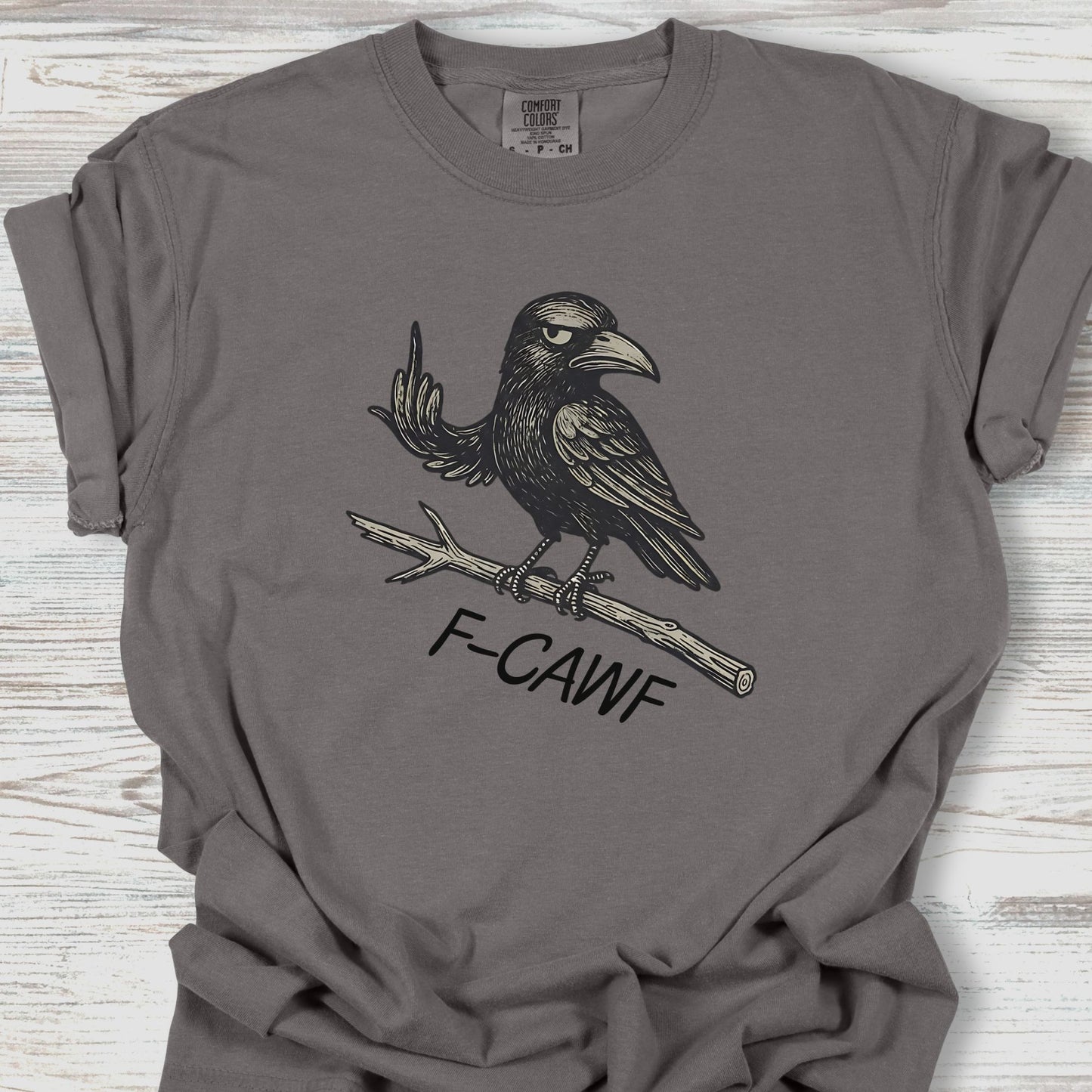 Gray t-shirt with a crow graphic and 'F-CAWF' text on a wooden surface