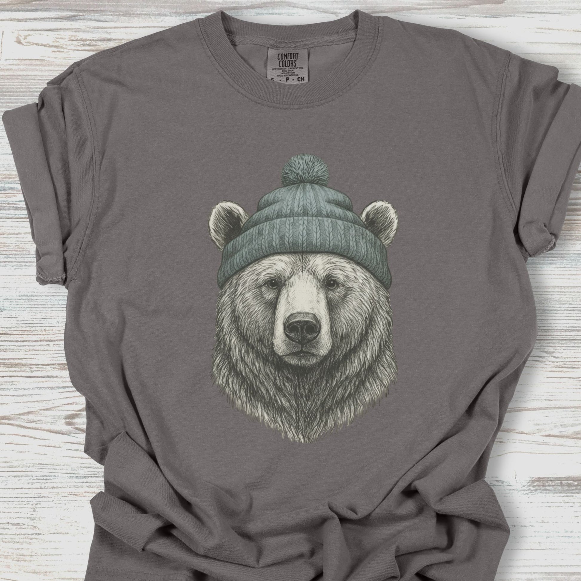 Gray t-shirt with a bear wearing a green beanie on a wooden surface