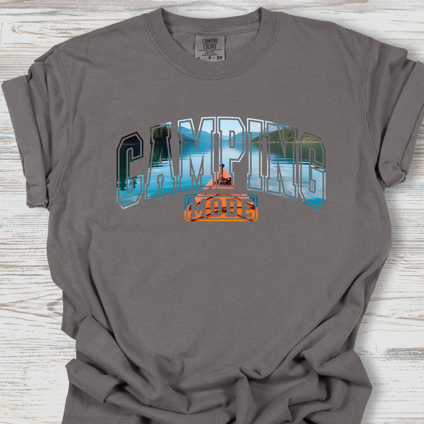 Gray t-shirt with 'Camping' graphic design on a wooden surface