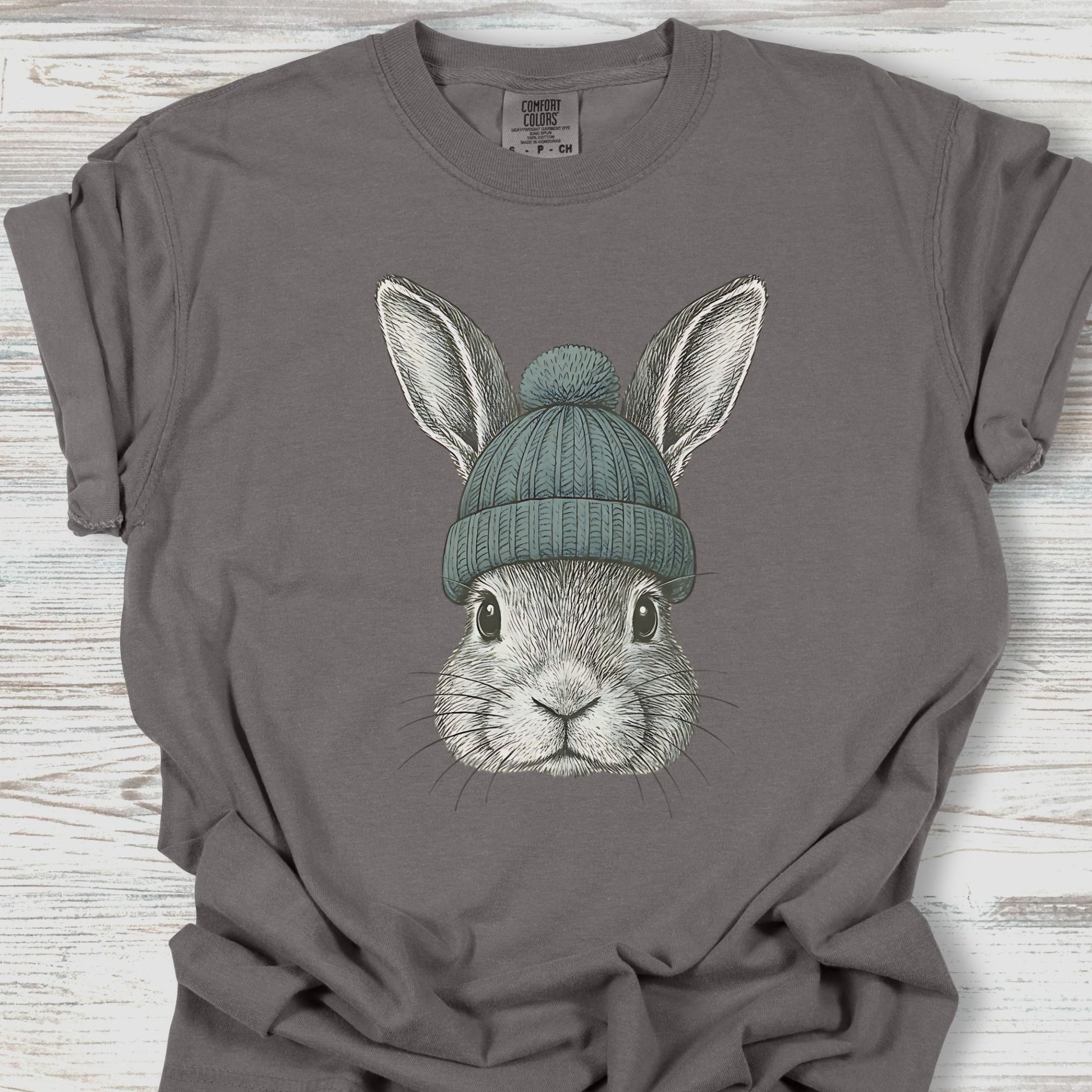 Gray t-shirt with a graphic of a rabbit wearing a green beanie on a wooden surface
