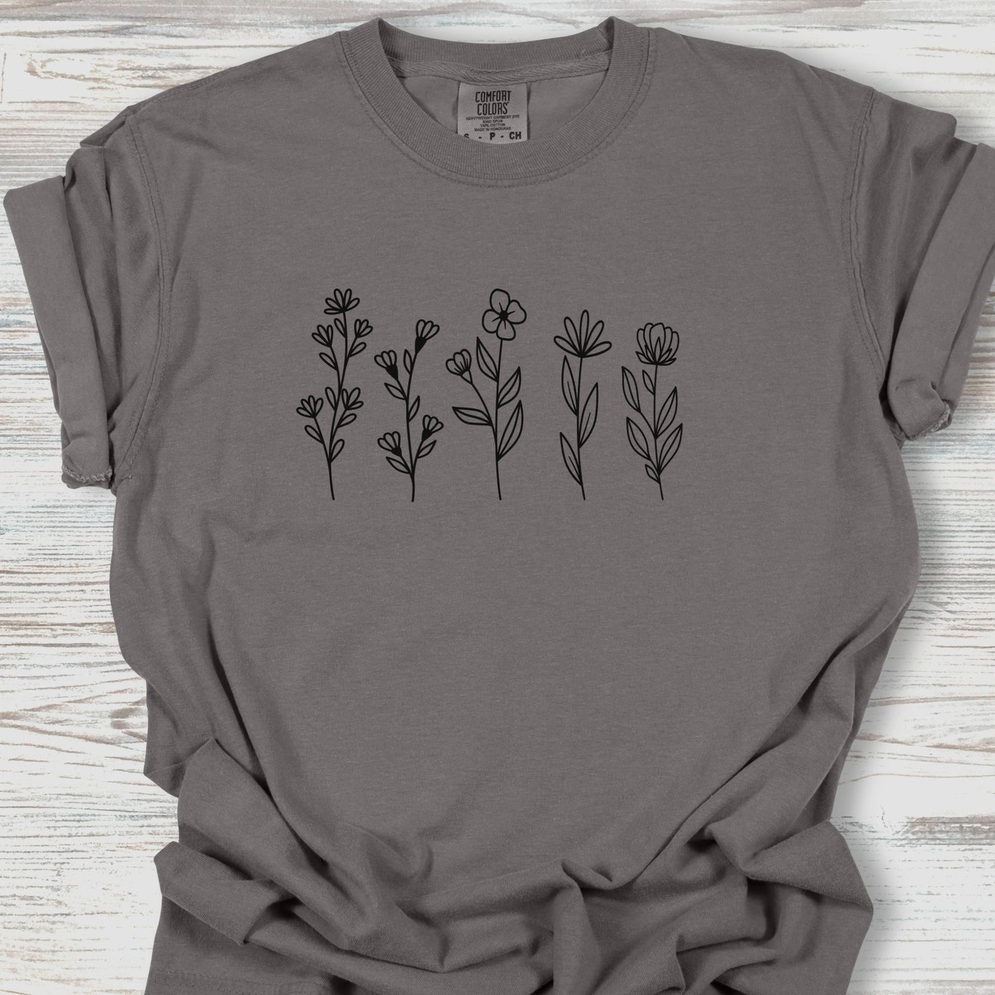 Gray t-shirt with black floral designs on a wooden surface