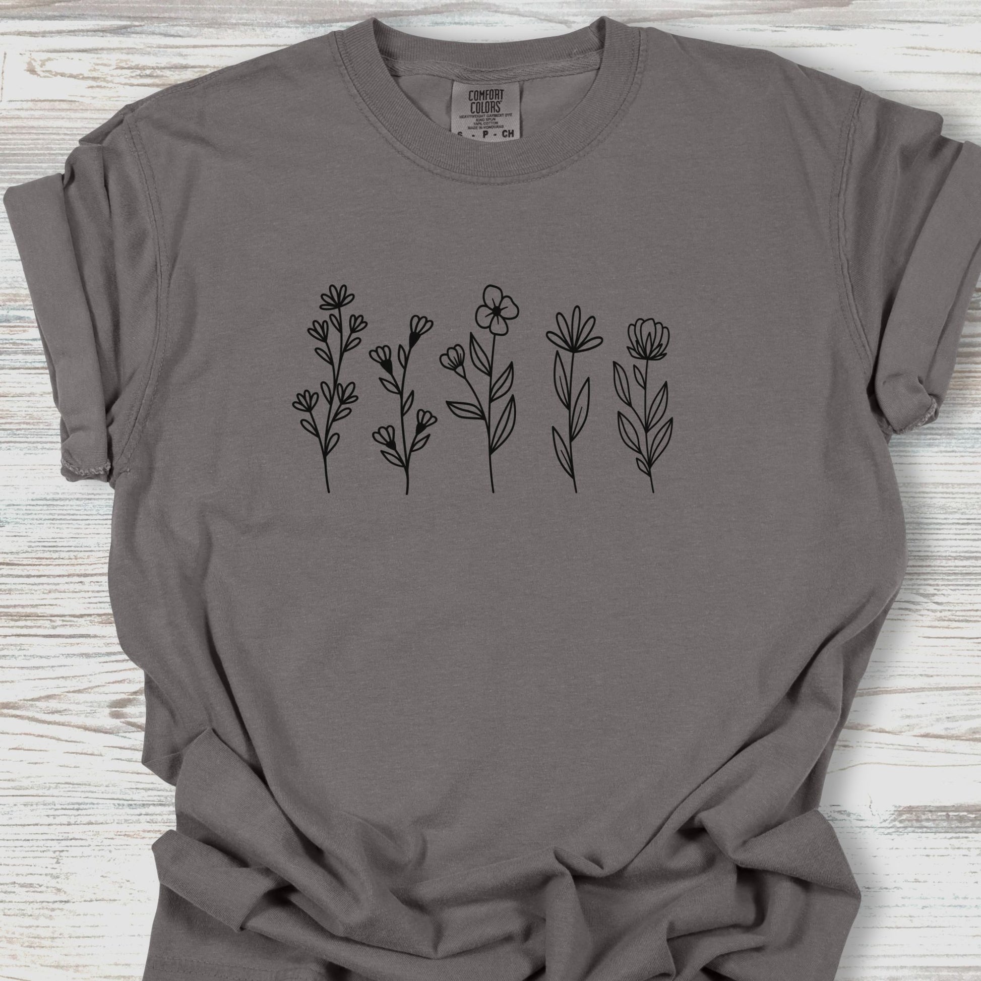 Gray t-shirt with black floral designs on a wooden surface
